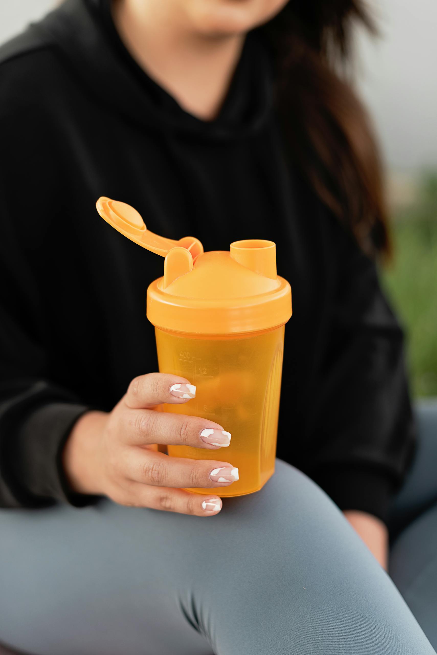 Close-up of a woman holding an orange shaker bottle. Ideal for fitness and hydration themes.